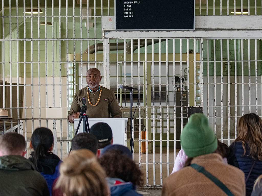 Troy Williams, formerly incarcerated speaker and founder of Restorative Media Inc., gives a talk before an audience in the dining hall at Alcatraz. Photo by Dave Rauenbuehler.